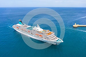 Cruise liner ship sails into the sea in the bay next to the lighthouse, aerial view