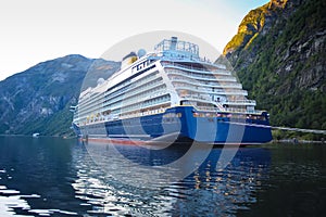 Cruise ship at anchor on a beautiful summer day. Reflections of the mountains in the fjord. Lush green landscape.