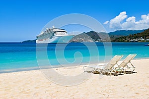 Cruise ship in Caribbean Sea with beach chairs on white sandy beach. Summer travel concept.