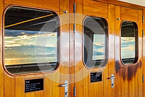 Cruise ship heavy varnished wood exterior doors with windows reflecting the sea.