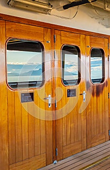 Cruise ship heavy varnished wood exterior doors with windows reflecting the sea.