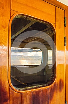 Cruise ship heavy wooden varnished exterior door with window reflecting the sea.