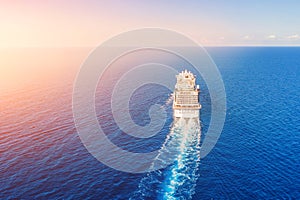 Cruise ship liner goes into horizon the blue sea leaving a plume on the surface of the water seascape during sunrise. Aerial view