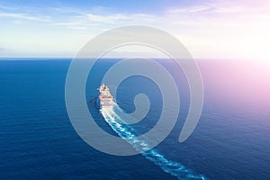 Cruise ship liner goes into horizon the blue sea leaving a plume on the surface of the water seascape during sunrise. Aerial view