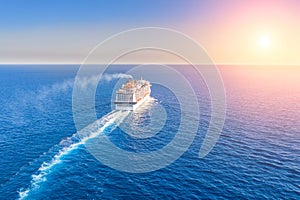 Cruise ship liner goes into horizon the blue sea leaving a plume on the surface of the water seascape during sunset. Aerial view,