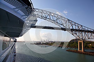 Cruise ship passing under the Bridge of the Americas, with a major shipping port in the background, Panama Canal