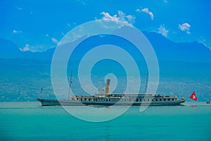 A cruise ship for tourists is sailing on the lake of Geneva in Lausanne, Switzerland. With the blue mountains as the background