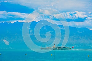 A cruise ship for tourists is sailing on the lake of Geneva in Lausanne, Switzerland. With the blue mountains as the background