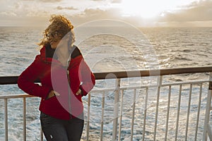 Cruise ship vacation woman enjoying sunset on travel at sea. Traveler happy woman in red jacket looking at ocean relaxing on