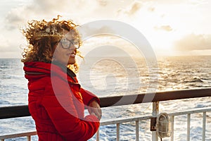 Cruise ship vacation woman enjoying sunset on travel at sea. Traveler happy woman in red jacket looking at ocean relaxing on