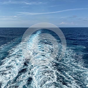 Cruise ship wake on a beautiful sunny day with white clouds and blue seas