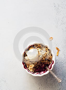 Crumble with berries, apples, ball of ice cream and almond in white bowl close up