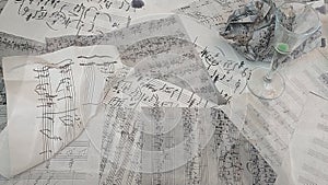 Crumbled Handwritten music notes on white paper with empty glass of alcohol