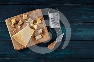 Crumbled Parmesan cheese with a knife and a grater, shot from the top on a dark wooden background