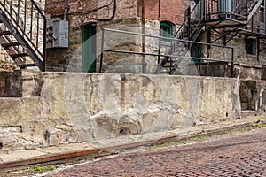 Crumbling concrete wall alongside a red brick street, brick apartment building behind