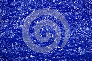 Crumpled cellophane bright blue transparent plastic paper texture abstract background.