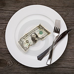 Crumpled dollar in the plate with fork and knife on the wooden