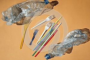Crumpled empty transparent plastic bottles from water, plastic forks and straws on a brown background