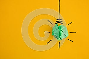 Crumpled green paper light bulb on yellow background