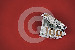 crumpled hundred dollar bill lying on a red background