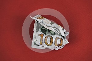 crumpled hundred dollar bill lying on a red background