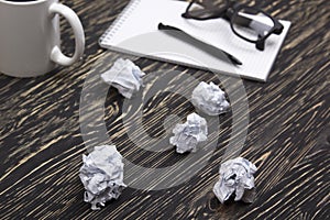 Crumpled paper balls with eye glasses mug, pen and notebook