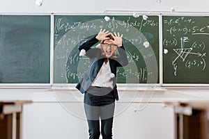 Crumpled paper balls flying at frightened female teacher in classroom with chalkboard