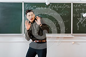 Crumpled paper balls flying at frightened male teacher in classroom with chalkboard