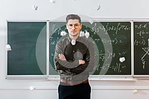 Crumpled paper balls flying at male teacher with arms crossed in classroom with chalkboard