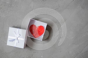 Crumpled paper heart in gift box in the hand against the concrete floor.  Broken relationships in bad Valentine`s day. concept.