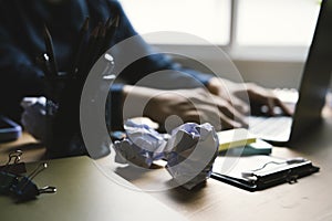 Crumpled paper on office desk with businessman working with laptop.