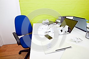 Crumpled paper over laptop on desk with empty chair and folders