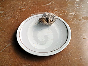 Crumpled paper on a white plate put on a dirty wooden table