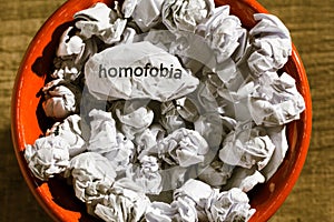 Crumpled paper written homofobia, portuguese and spanish word for homophobia, inside the trash can. Paper balls. Concept of old photo