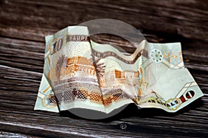 Crumpled Saudi Arabia money of 10 SAR ten riyals isolated on wooden background, wrinkled 10 Saudi Riyals cash bill banknote