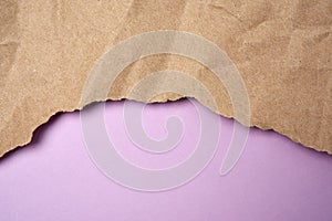 Crumpled sheet of brown wrapping paper with torn edges on a purple background