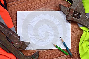 A crumpled sheet of paper with two pencils surrounded by green and orange working uniforms and adjustable wrenches. Still life as