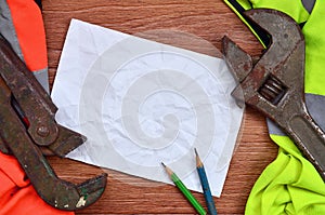A crumpled sheet of paper with two pencils surrounded by green and orange working uniforms and adjustable wrenches. Still life as