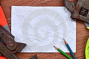 A crumpled sheet of paper with two pencils surrounded by green and orange working uniforms and adjustable wrenches. Still life as