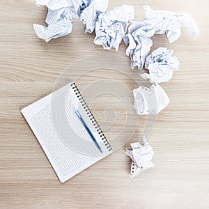 crumpled sheets of paper next to a notepad and a ballpoint pen on a wooden table.