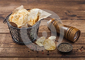 Crunchy potato crisps chips snack with black pepper in wooden bowl on dark background with mill and ground pepper