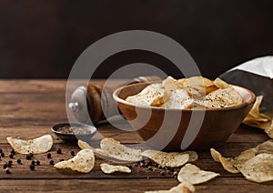 Crunchy potato crisps chips snack with black pepper in wooden bowl on dark background with mill and ground pepper