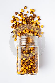 Crunchy Roasted Chana Masala spilled out and in a glass jar, made with Bengal Grams or Chickpeas.