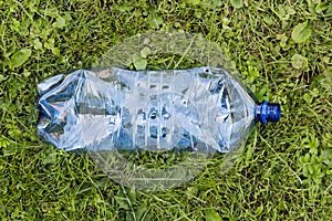 Crushed blue plastic bottle laying in grass. Pollution and environment concept