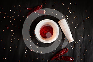 Crushed chili powder in mortar with pestle and dried red chilies isolated on black background.