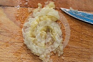 Crushed garlic cloves are salted on a wooden cutting board