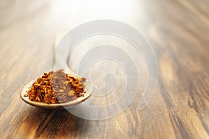 Crushed hot red cayenne peppers on a wooden spoon. Horizontal photo with plenty of empty space.
