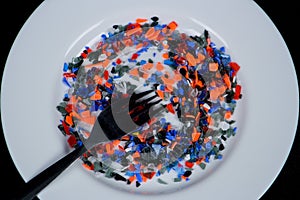 Crushed multicolored plastic pieces on white plate and fork.