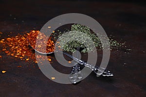 crushed red pepper and dried mint in spoons on dark rustic background