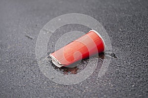 Crushed soda cup thrown on ground on asphalt road. Plastic wast destroying the planet